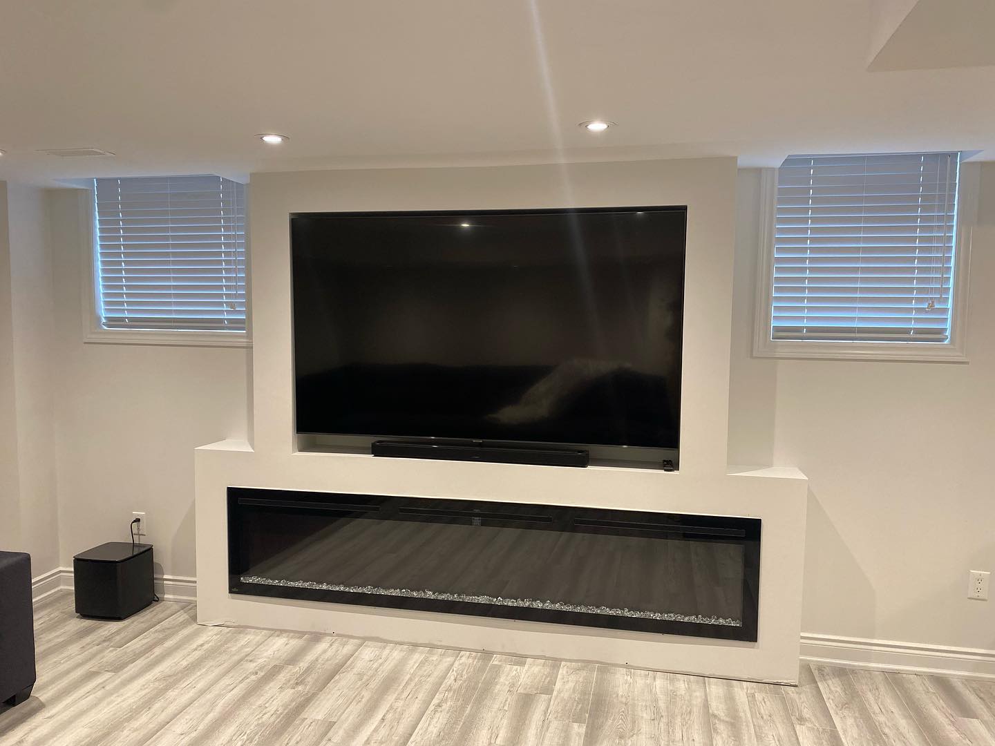 Completed basement feature wall with recessed television and linear fireplace