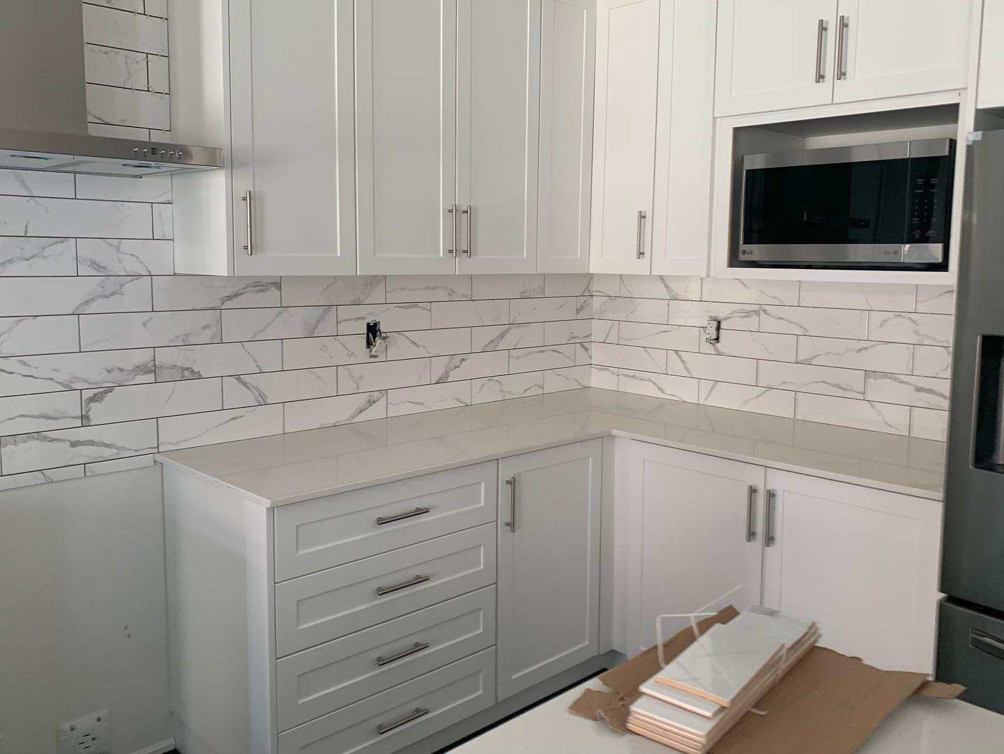 White kitchen cabinetry with newly installed marble-look tile backsplash